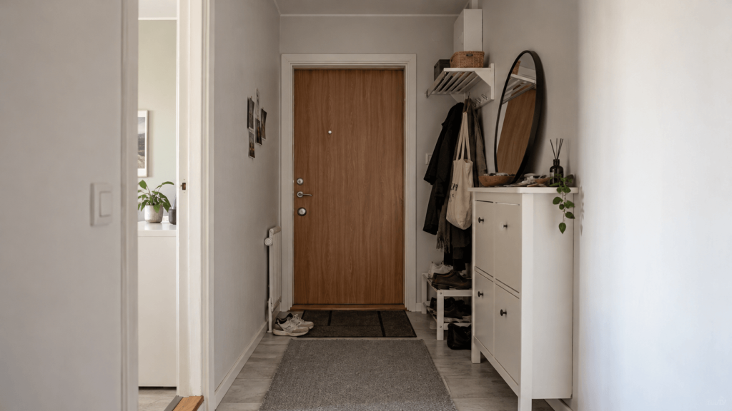 Narrow rental apartment hallway with a shallow white shoe cabinet and neutral runner rug.