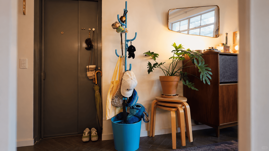 Blue freestanding coat rack holding bags and accessories beside an apartment entry door.