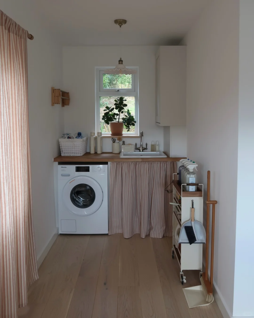 Narrow utility laundry room with a washer, wood countertop, striped storage curtain, and slim rolling cart.